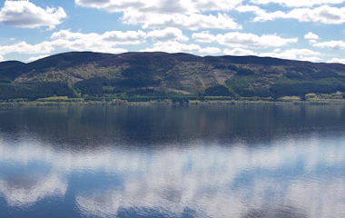 Panoramaudsigt over Loch Ness med perfekte skyrefleksioner på det rolige vand i de skotske højlande