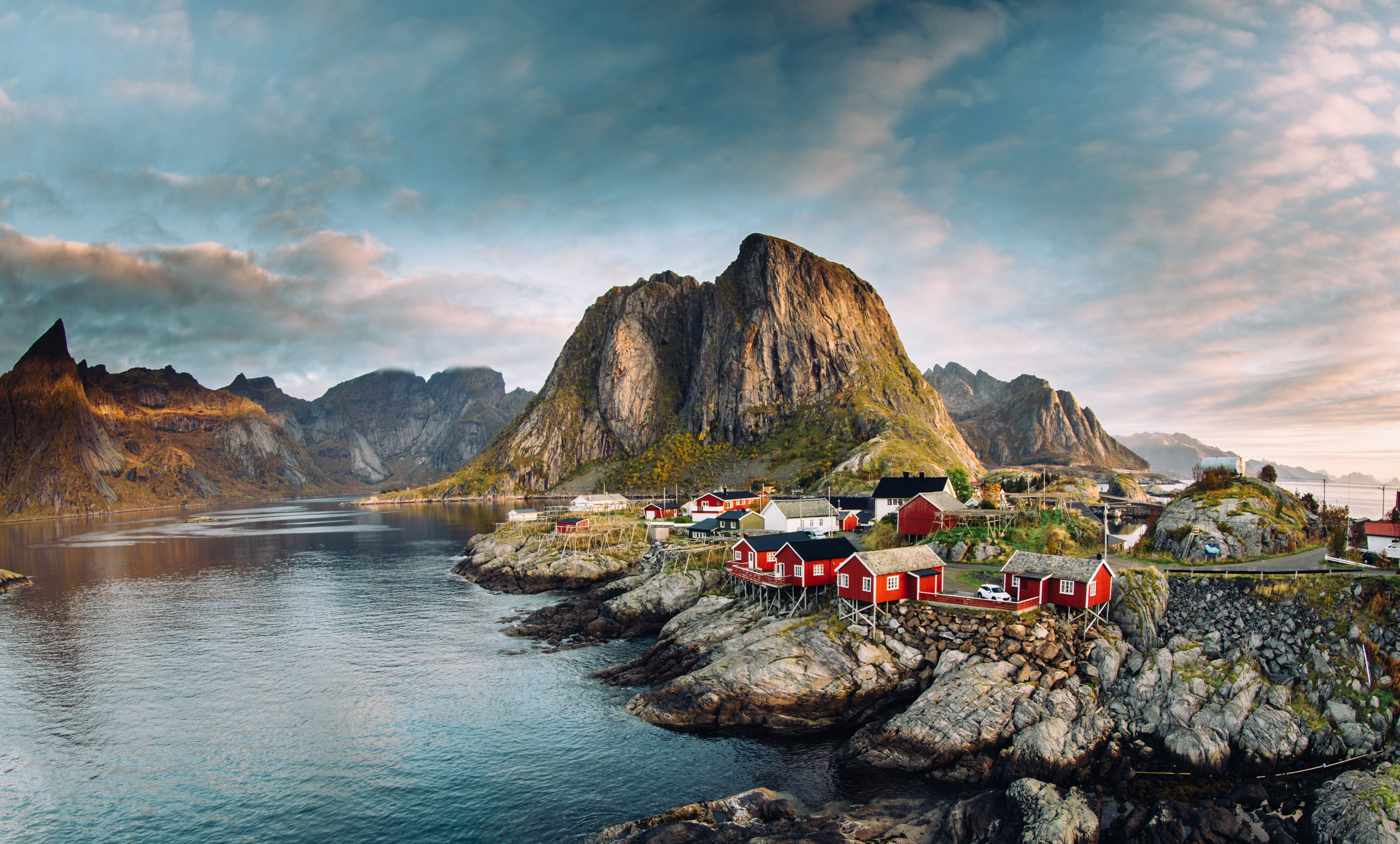 Idyllisk fiskerlandsby med traditionelle rode hytter mellem majestætiske bjergtinder og fjord ved solnedgang i Reine, Lofoten, Norge