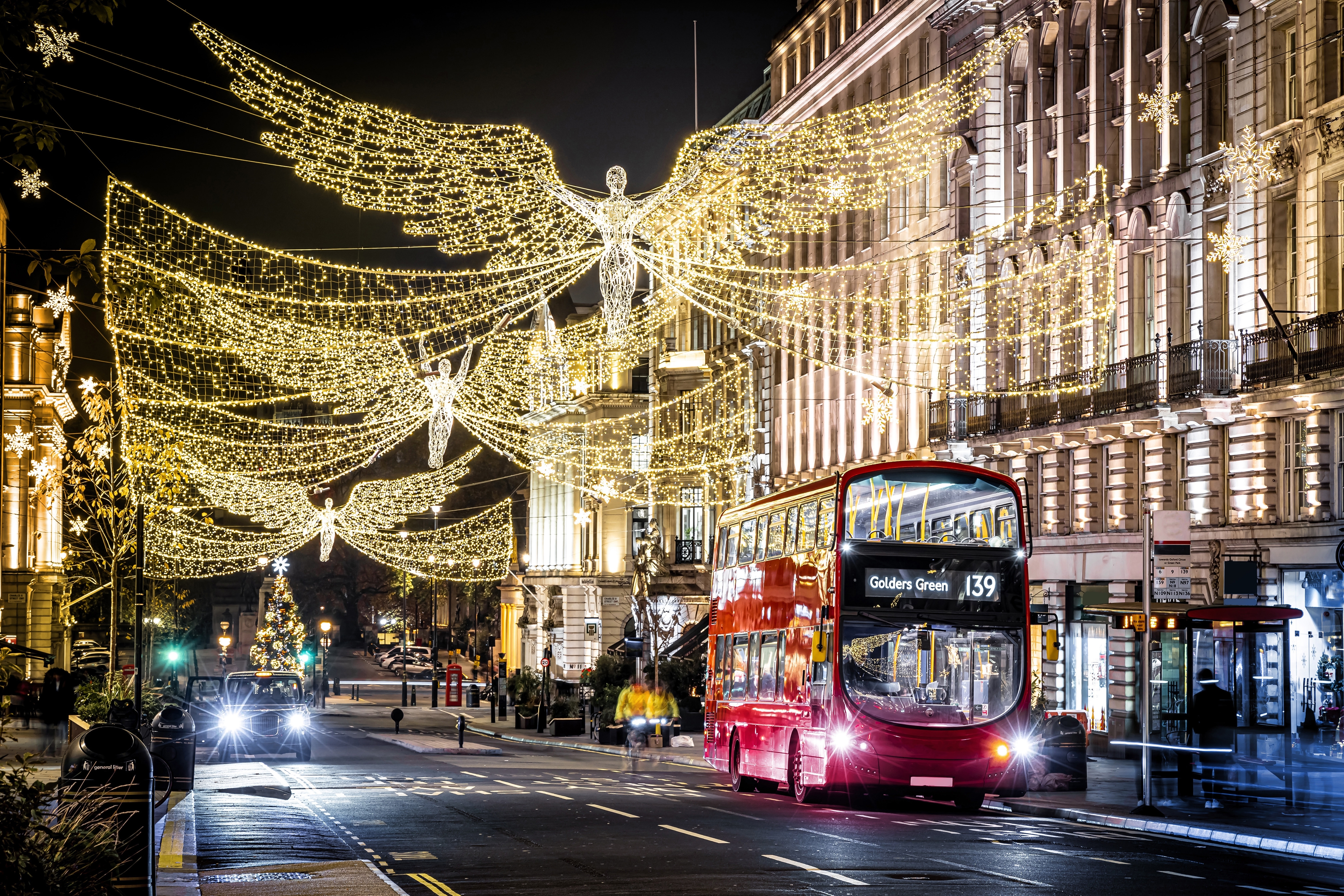Regent Street i London pyntet med strålende julelys formet som engle og en rød dobbeltdækker bus om natten