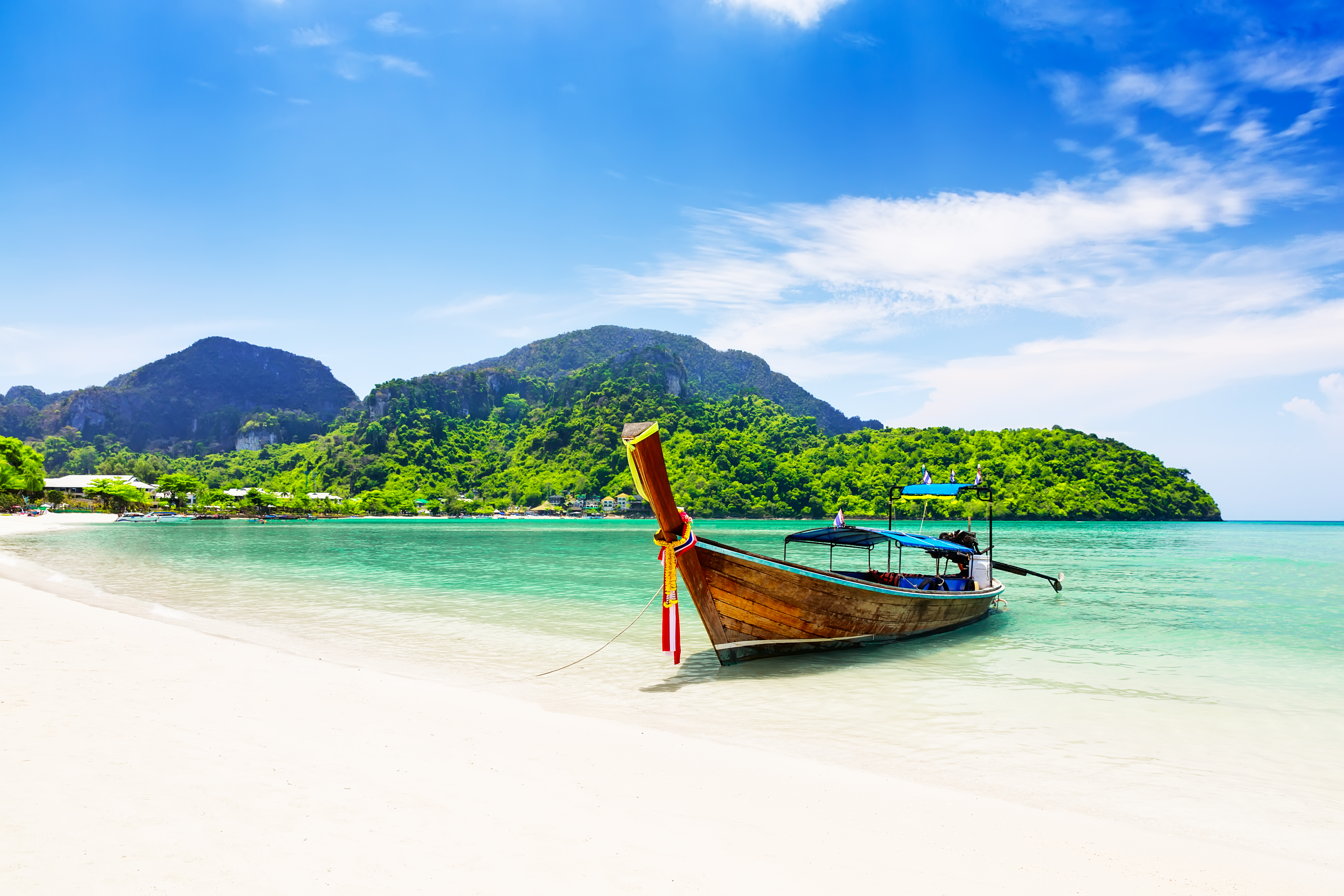 Traditionel longtail båd på hvid sandstrand med turkisblåt vand og grønne bjerge i Thailand