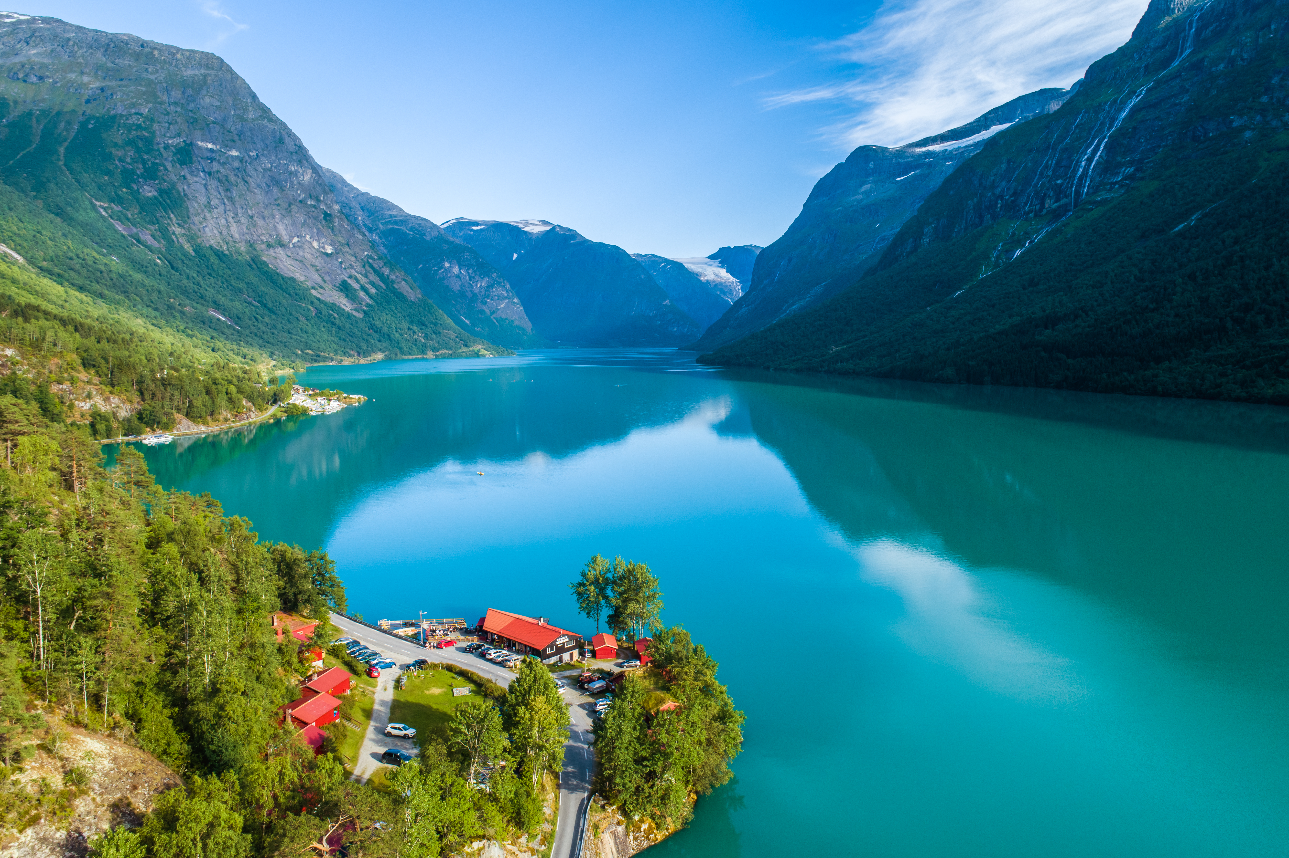 Luftfoto af den smukke Lovatnet sø i Norge med turkis vand, dramatiske bjerge og lille landsby med røde tage