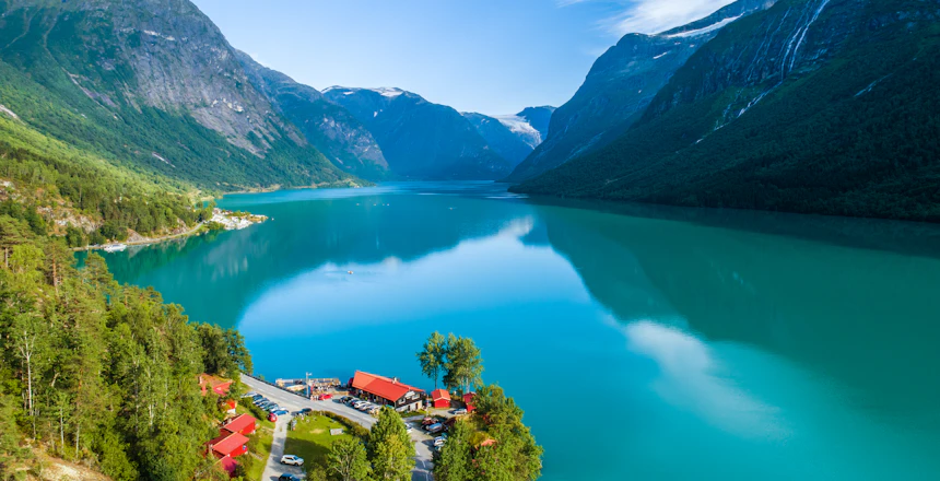 Luftfoto af den smukke Lovatnet sø i Norge med turkis vand, dramatiske bjerge og lille landsby med røde tage