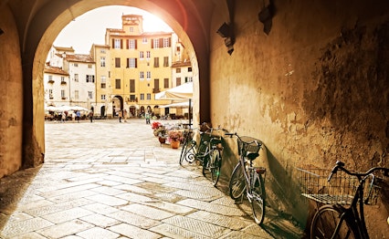Den ovale Amfiteaterplads i Lucca, Toscana, badet i gyldent solnedgangslys der oplyser de farverige historiske bygninger bygget på resterne af et romersk amfiteater