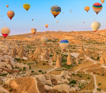 Farverige luftballoner svæver over Göremes karakteristiske klippeformationer i Kappadokien, Tyrkiet, under en spektakulær solopgang i Rose Valley