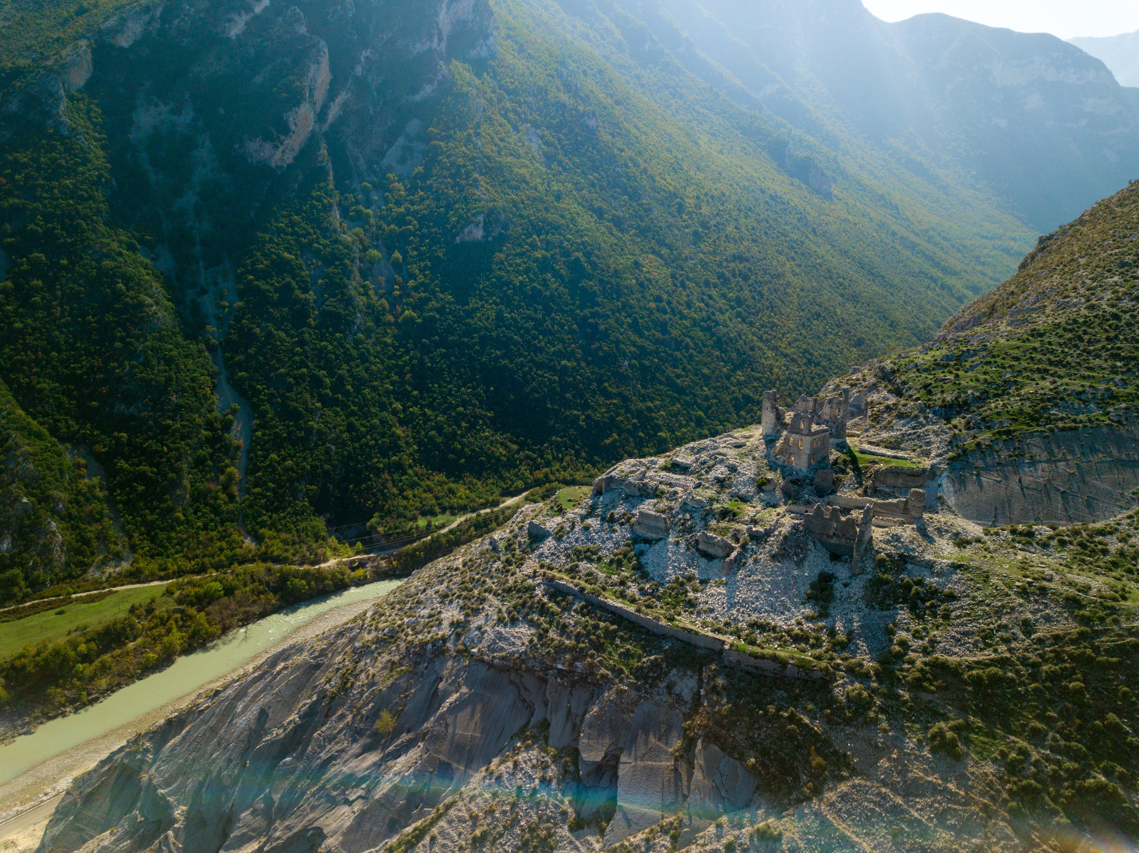 Dramatisk luftfoto af de historiske Ali Bej ruiner i Kelcyre, Albanien, omgivet af majestætiske bjerge og grøn natur i Permet-regionen