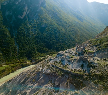 Dramatisk luftfoto af de historiske Ali Bej ruiner i Kelcyre, Albanien, omgivet af majestætiske bjerge og grøn natur i Permet-regionen