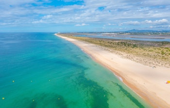 Luftfoto af den idylliske Ilha de Tavira strand med parasol og solsenge langs Algarvekysten i Portugal