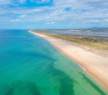 Luftfoto af den idylliske Ilha de Tavira strand med parasol og solsenge langs Algarvekysten i Portugal