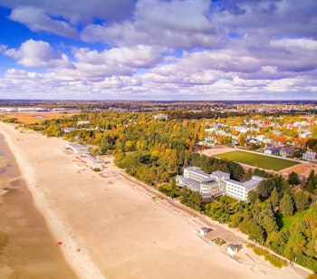 Luftfoto af den gyldne sandstrand i Pärnu, Estlands sommerhovedstad, med smuk kystlinje og farverige efterårstræer under en dramatisk himmel
