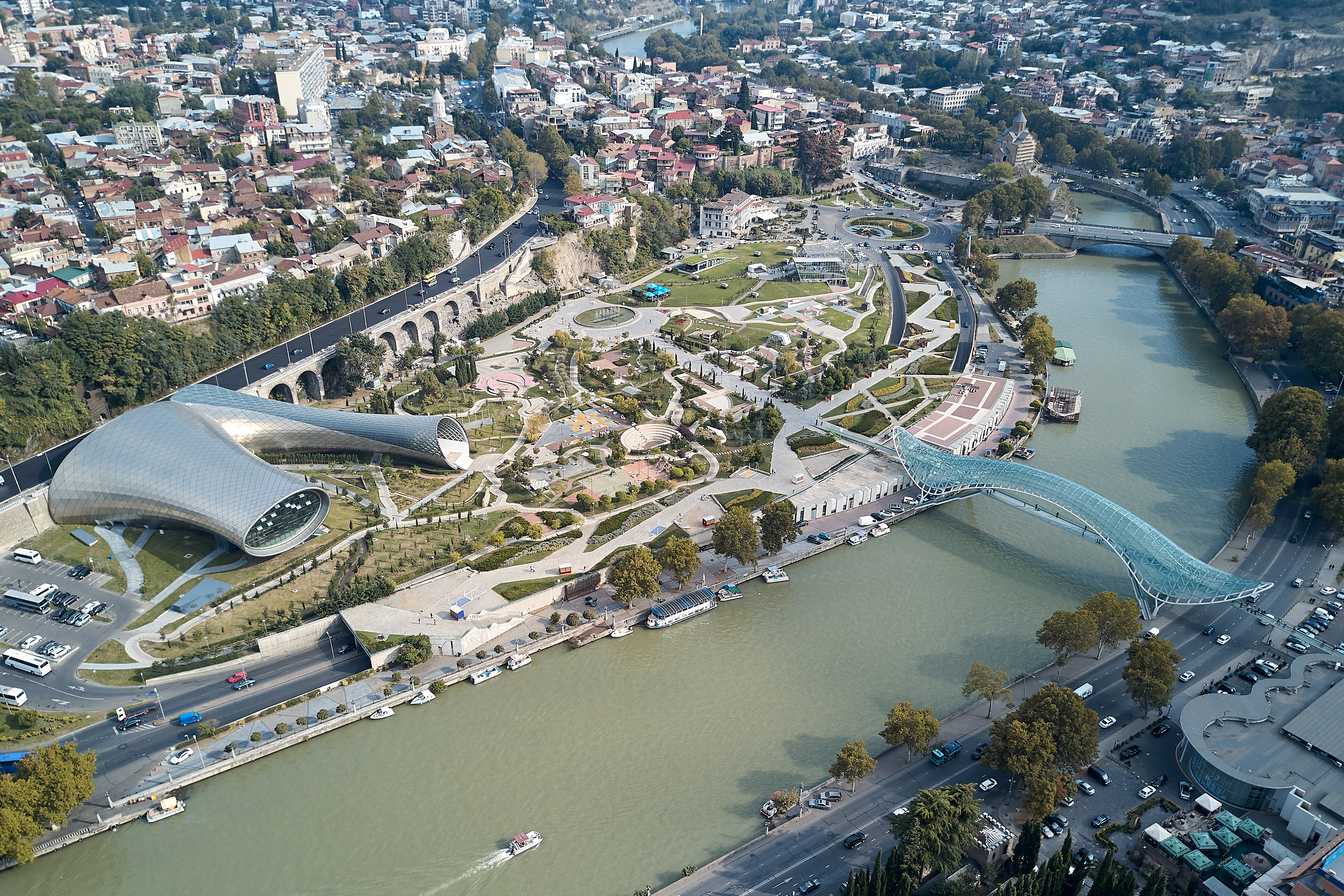 Luftfoto af Tbilisi med den historiske gamle bydel, Kura-floden og Fredsbygningen omkranset af bjerge i Georgien