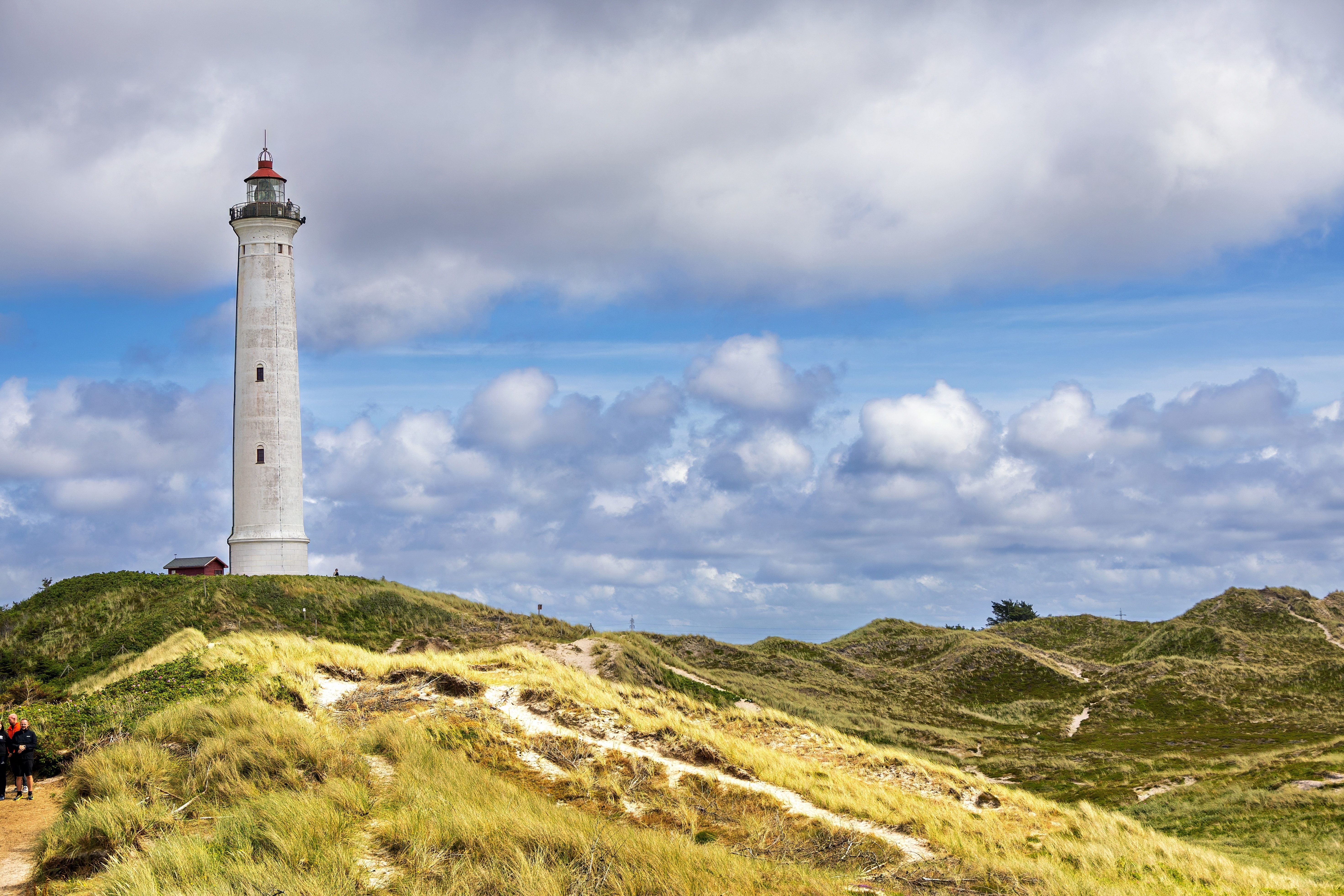 Lyngvig Fyr fyrtårn rejser sig over de grønne klitter ved Hvide Sande på Jyllands vestkyst under en dramatisk skyet himmel
