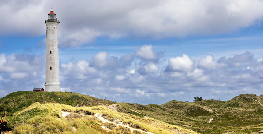Lyngvig Fyr fyrtårn rejser sig over de grønne klitter ved Hvide Sande på Jyllands vestkyst under en dramatisk skyet himmel