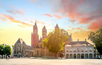 Vrijthof-pladsen i Maastricht ved solnedgang med den historiske Sankt Servatius Basilika og rådhuset under en dramatisk gylden himmel