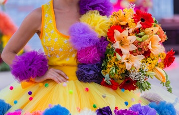 Smilende kvinde iført farverig blomsterdragt under den traditionsrige Blomsterfestival (Festa da Flor) i Funchal på Madeira, hvor øens rige kulturarv fejres med festlige parader