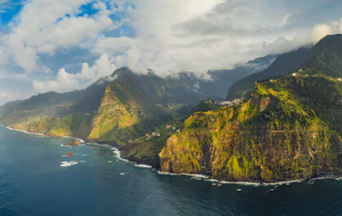 Spektakulær luftfoto af Madeiras dramatiske kystlinje med gyldne klipper og blåt ocean ved solnedgang