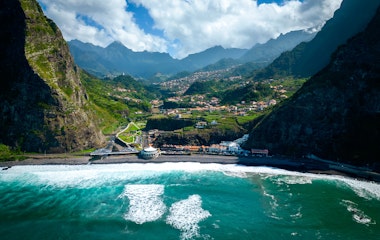 Betagende luftfoto af São Vicente på Madeira med sort sandstrand, brusende atlanterhavsbølger og dramatiske bjerge i baggrunden