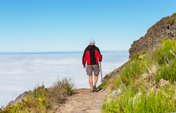 Vandrer på bjergsti over skyerne på Madeira med udsigt til det naturskønne landskab, perfekt til aktive rejseoplevelser og vandreture.