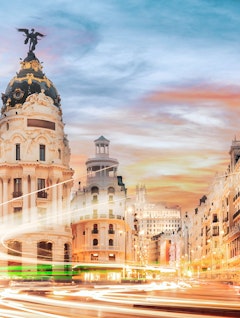 Den berømte Gran Via i Madrid ved solnedgang med historiske bygninger og dynamiske lysspor fra trafikken