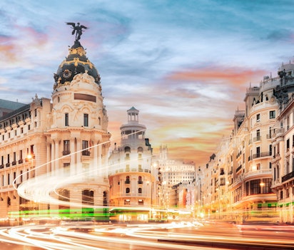 Den berømte Gran Via i Madrid ved solnedgang med historiske bygninger og dynamiske lysspor fra trafikken