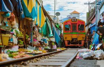 Farverigt tog kører langsomt gennem det berømte Maeklong jernbanemarked i Thailand, hvor sælgere og friske grøntsager ligger langs sporene nær Bangkok