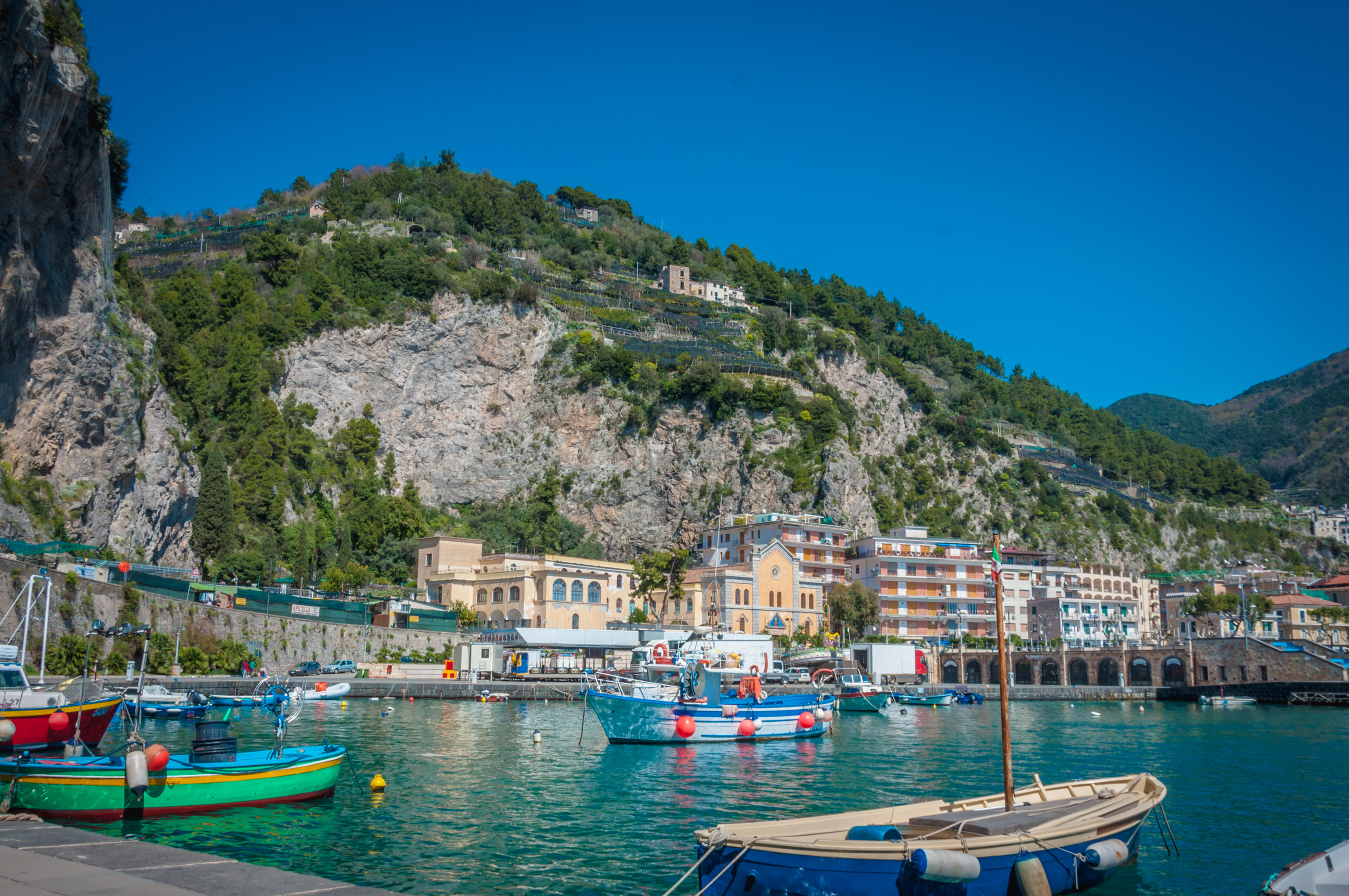 Farverige fiskerbåde i havnen i Maiori på den smukke Amalfikyst i Italien med dramatiske klipper og grønne terrasser i baggrunden
