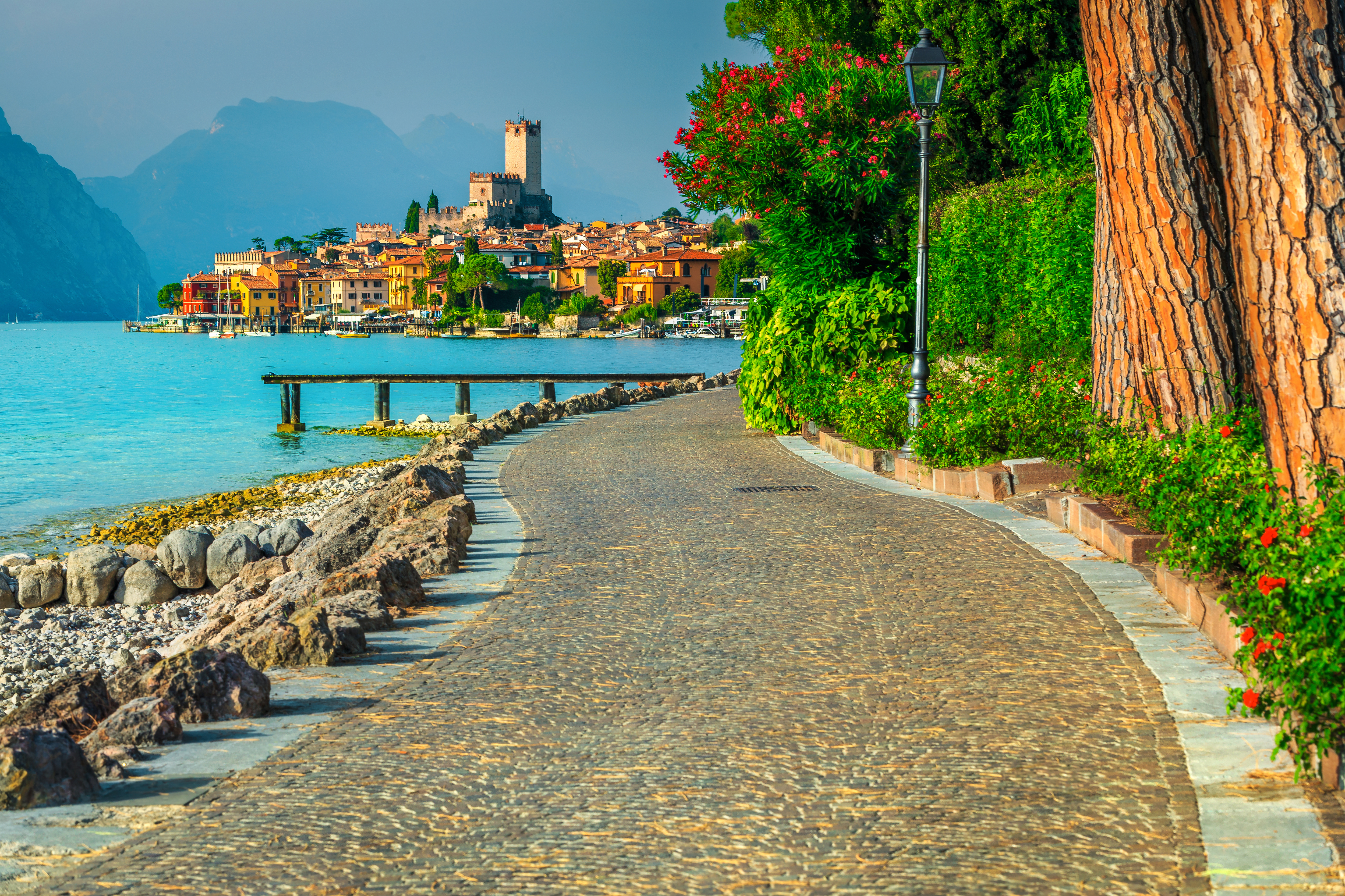 Smuk strandpromenade i Malcesine ved Gardasøen med farverige bygninger og alpine bjerge