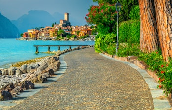 Smuk strandpromenade i Malcesine ved Gardasøen med farverige bygninger og alpine bjerge