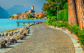 Smuk strandpromenade i Malcesine ved Gardasøen med farverige bygninger og alpine bjerge