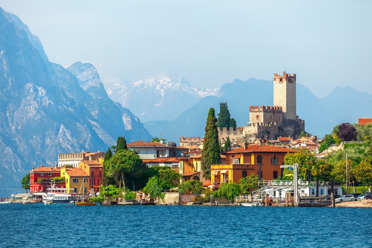 Idyllisk udsigt over Malcesine by med det historiske Scaliger-slot, farverige huse langs Gardasøens bred og sneklædte bjerge i baggrunden, Veneto-regionen, Italien