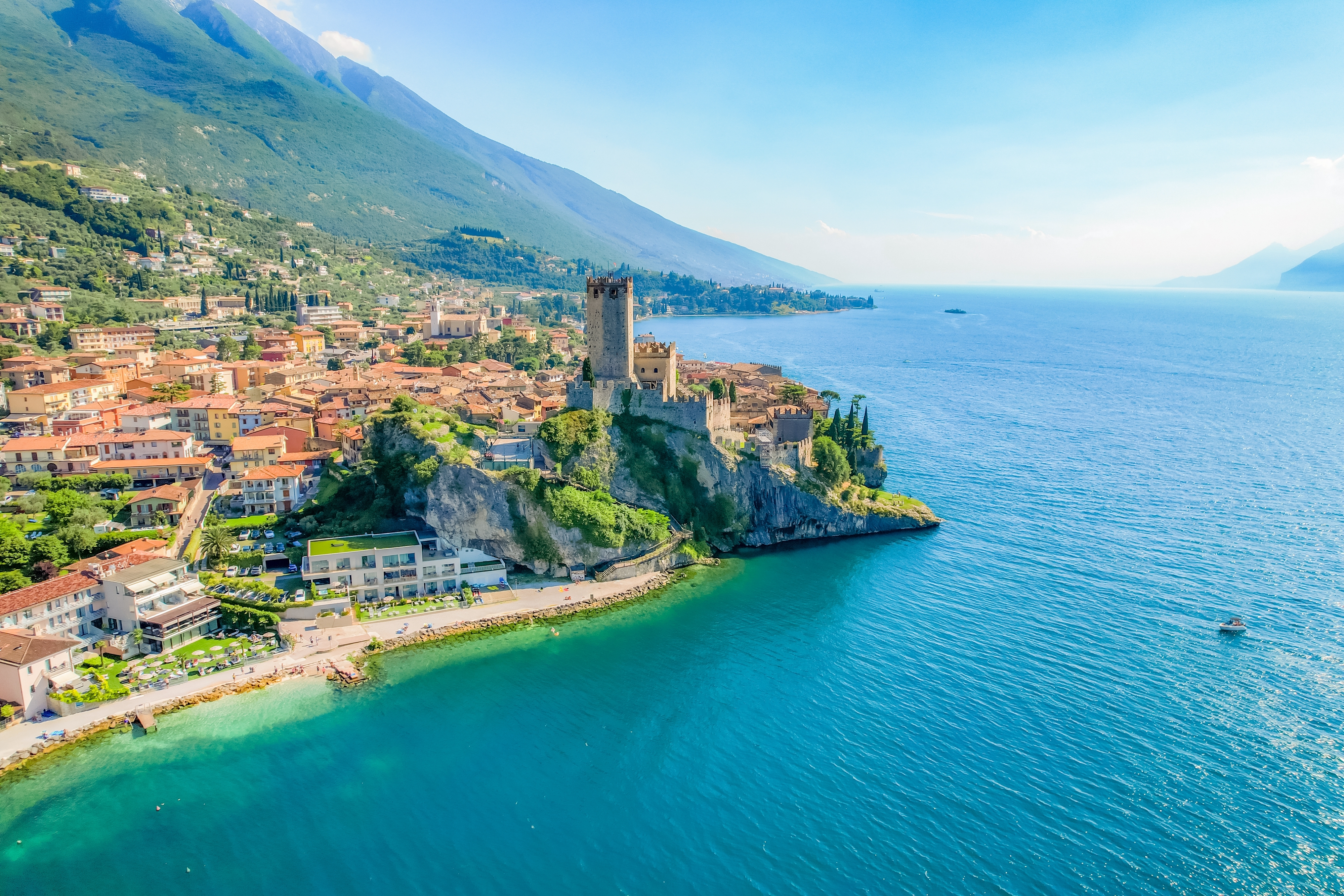 Luftfoto af Scaliger-slottet på klippen ved den turkisblå Gardasø i Malcesine, Italien, med alperne i baggrunden