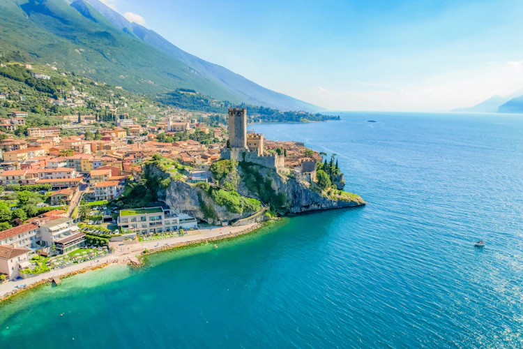 Luftfoto af Scaliger-slottet på klippen ved den turkisblå Gardasø i Malcesine, Italien, med alperne i baggrunden