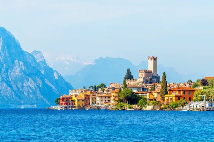 Historisk Scaliger-slot i Malcesine ved Gardasøens blå vand med farverige huse og sneklædte bjerge i baggrunden i Veneto-regionen