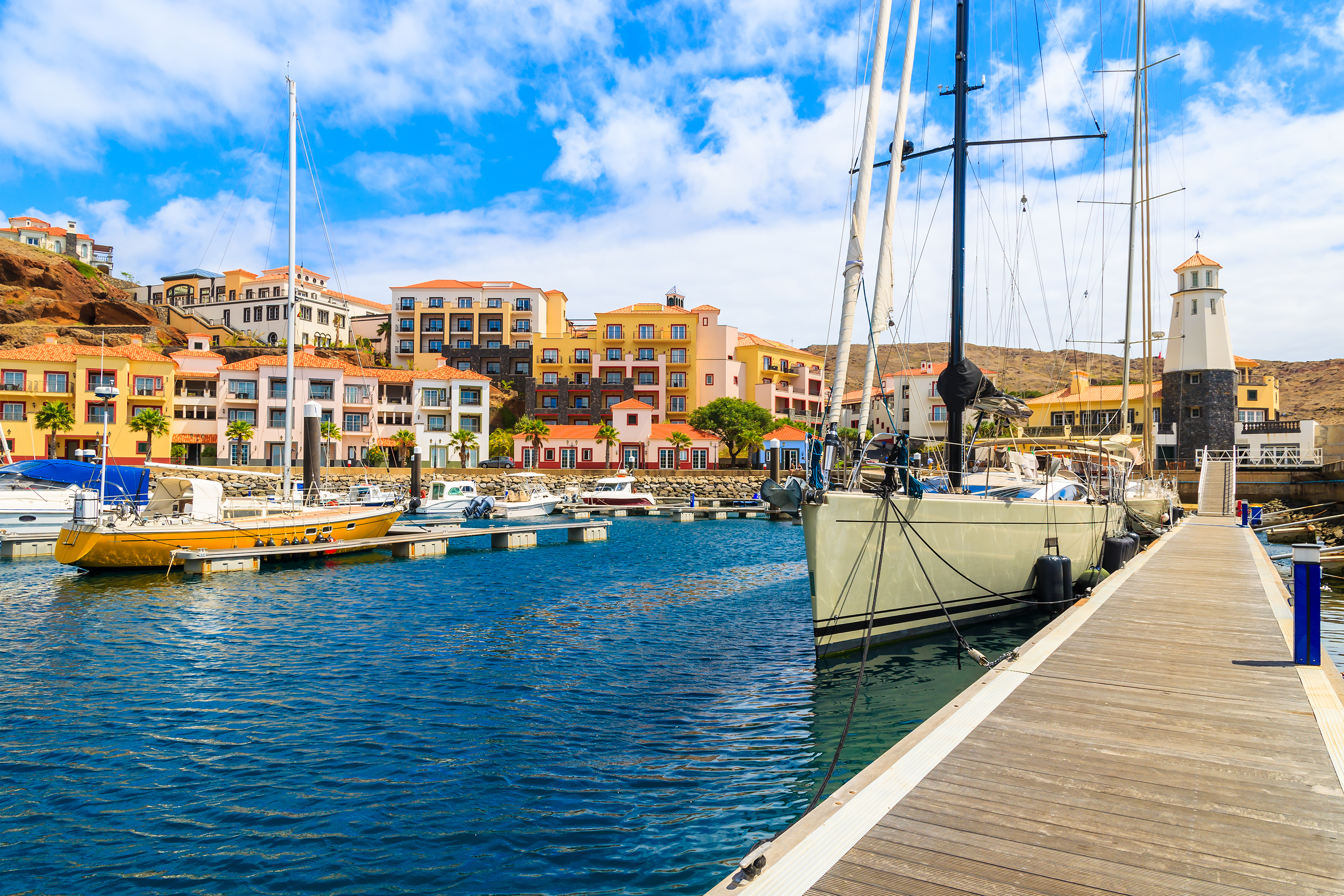 Idyllisk havnefront i Canical på Madeira med farverige sejlbåde fortøjet ved træbroen og charmerende farvede huse, der skaber den perfekte feriestemning ved Portugals kystlinje