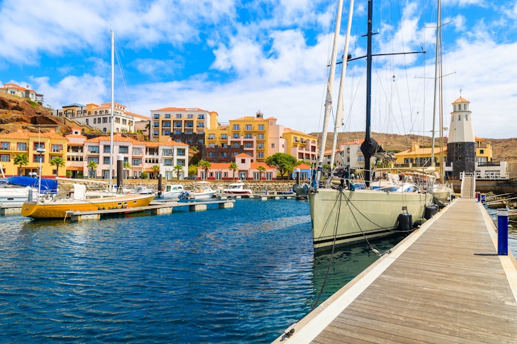 Idyllisk havnefront i Canical på Madeira med farverige sejlbåde fortøjet ved træbroen og charmerende farvede huse, der skaber den perfekte feriestemning ved Portugals kystlinje