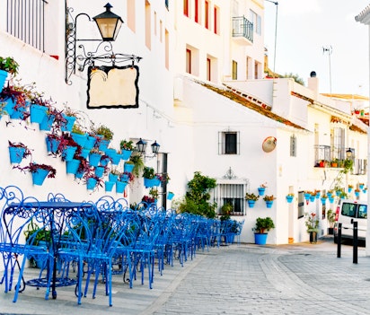 Charmerende gade i den hvide landsby Mijas med hvidkalkede huse, blå cafémøbler og farverige blomsterkrukker på væggene i Andalusien, Spanien