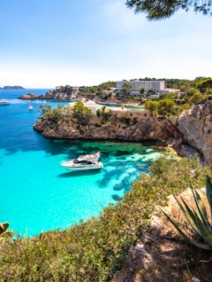 Betagende udsigt over den turkisblå bugt Cala Noelia på Mallorca med krystalklart vand, dramatisk klippekyst og både der sejler i bugten