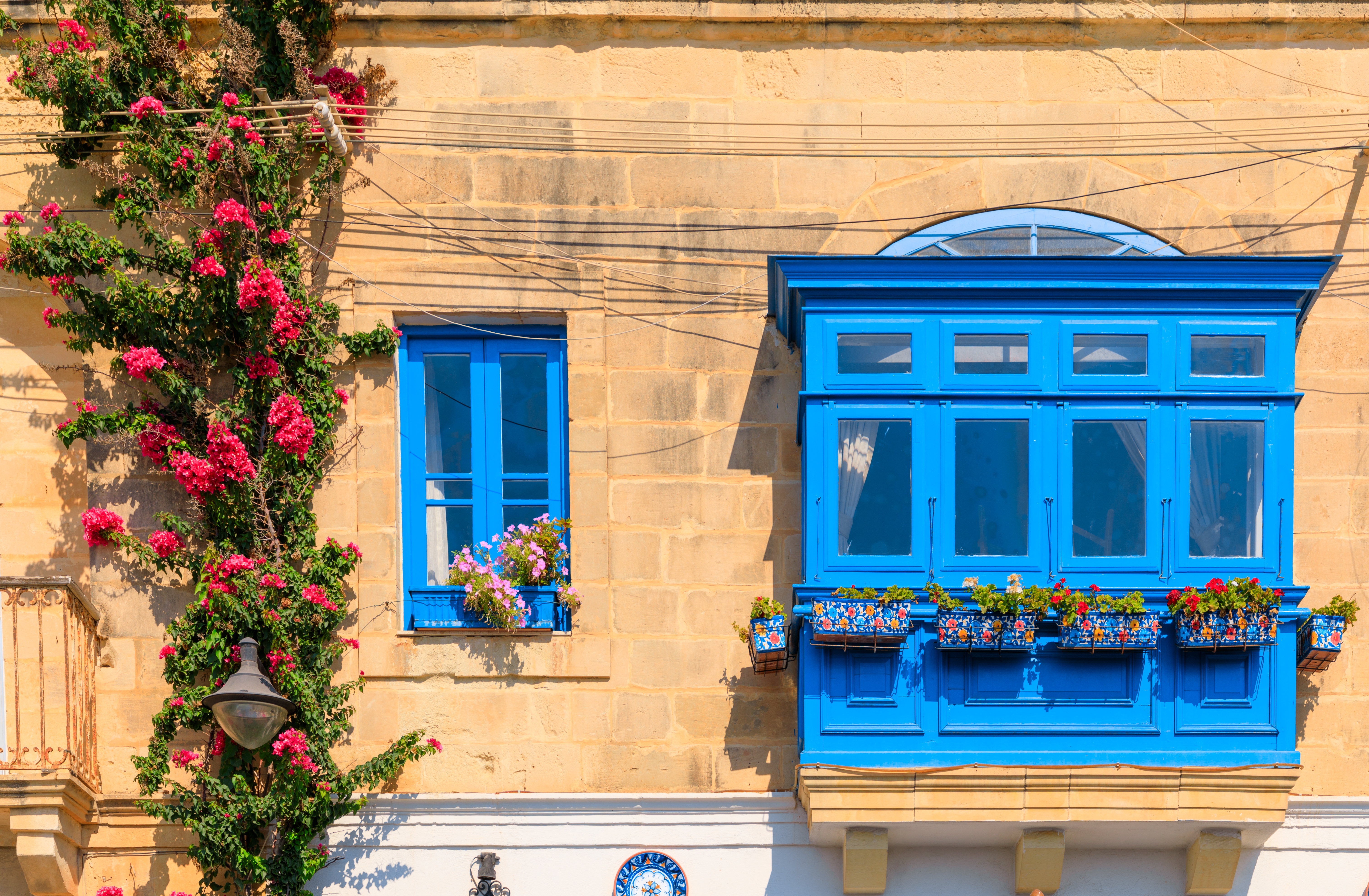 Traditionel blå træaltan kaldet Gallarija med farverige blomsterkasser på en gyldent kalkstens facade i Valletta, Malta