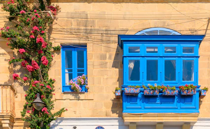 Traditionel blå træaltan kaldet Gallarija med farverige blomsterkasser på en gyldent kalkstens facade i Valletta, Malta