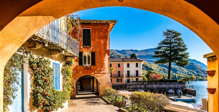 Charmerende udsigt gennem stenport til den maleriske by Mandello del Lario ved Comosøen med farverige bygninger og bjerge i baggrunden