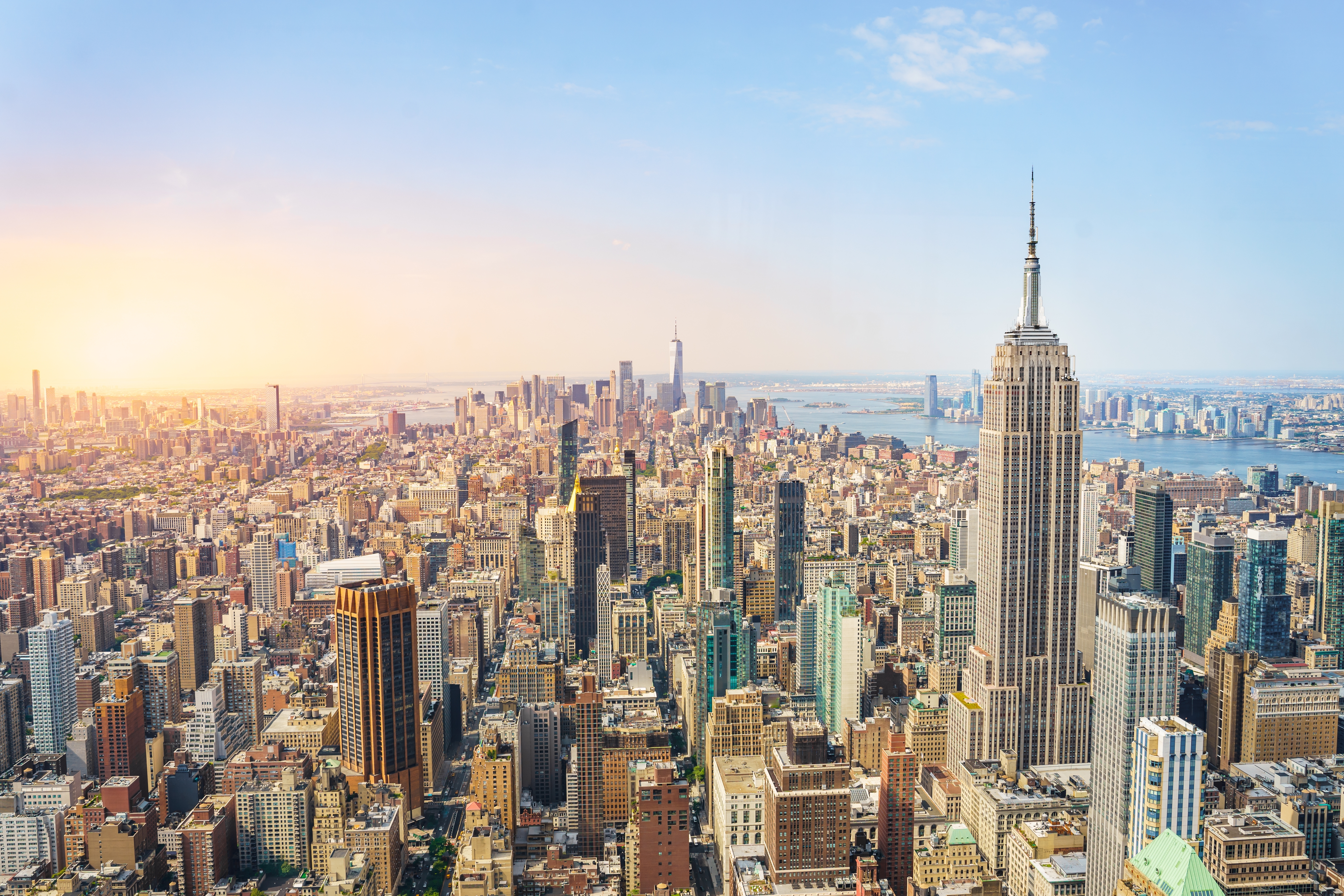 Imponerende panoramaudsigt over New Yorks skyline og Manhattan ved solnedgang med gyldent lys over byens skyskrabere