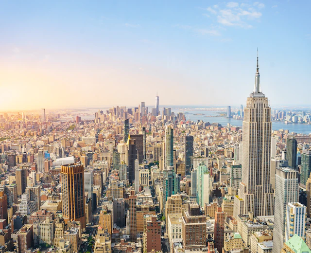 Imponerende panoramaudsigt over New Yorks skyline og Manhattan ved solnedgang med gyldent lys over byens skyskrabere