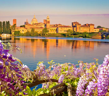 Smuk solnedgangsvisning af Mantuas historiske skyline spejlet i Lago Inferiore med lilla blomster i forgrunden