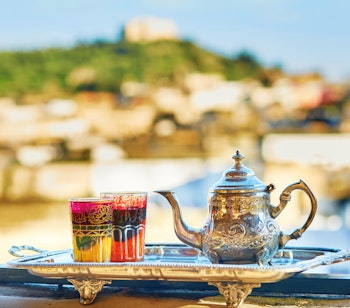 Autentisk marokkansk myntete serveret i farverige glas med en dekorativ sølvkande og traditionelle søde kager, der viser den ikoniske gæstfrihed i Marokkos medina-kvarterer