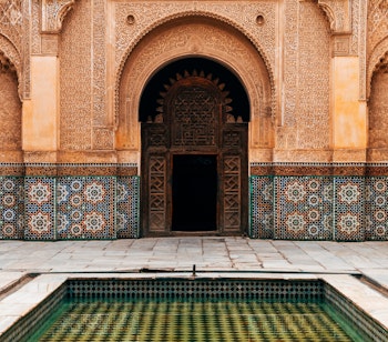 Traditionel marokkansk gårdhave i Marrakech med farverige mosaikmønstre på gulv og vægge - et smukt eksempel på islamisk arkitektur med elegante detaljer og håndværk
