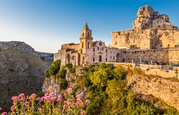 Historiske stenhuse og kirketårn i den gamle by Matera, Italien med blomster i forgrunden