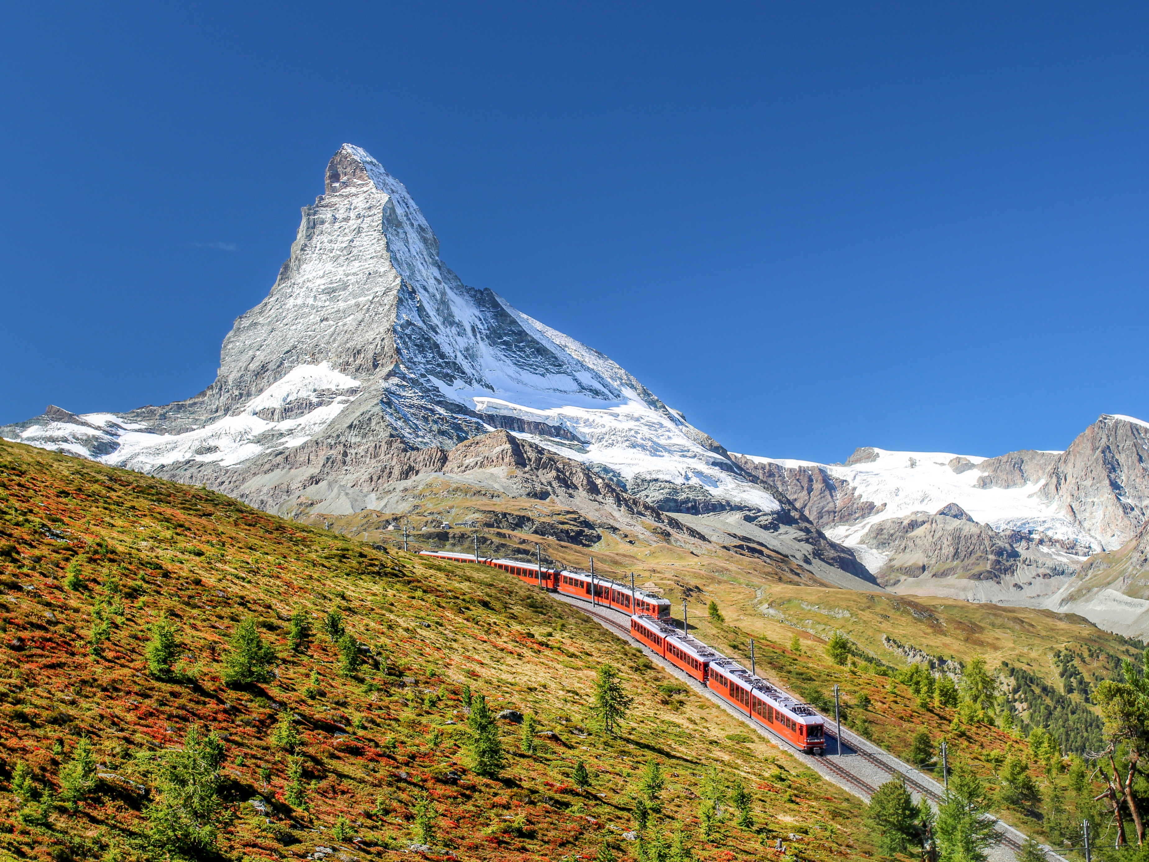 Tog kører gennem schweiziske alper med Matterhorn bjerg i baggrunden om efteråret