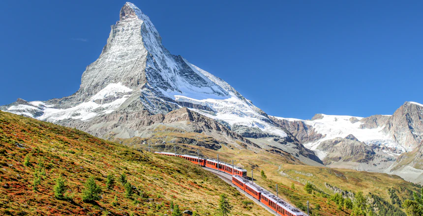 Tog kører gennem schweiziske alper med Matterhorn bjerg i baggrunden om efteråret
