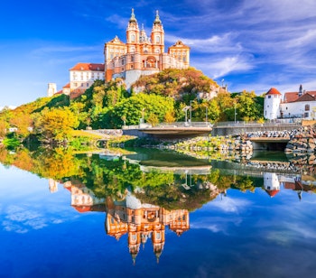 Det majestætiske Melk Kloster spejler sig i Donau-flodens vand på en solrig efterårsdag i den idylliske Wachau-dal i Østrig
