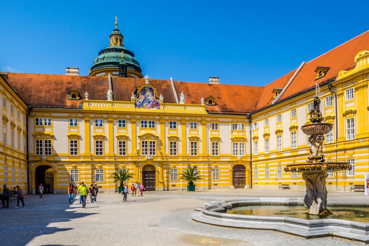 Imponerende gårdsplads i det gule barokke Melk Kloster i Østrig med flot fontæne og blå himmel, et UNESCO verdensarvssted i Wachau-regionen