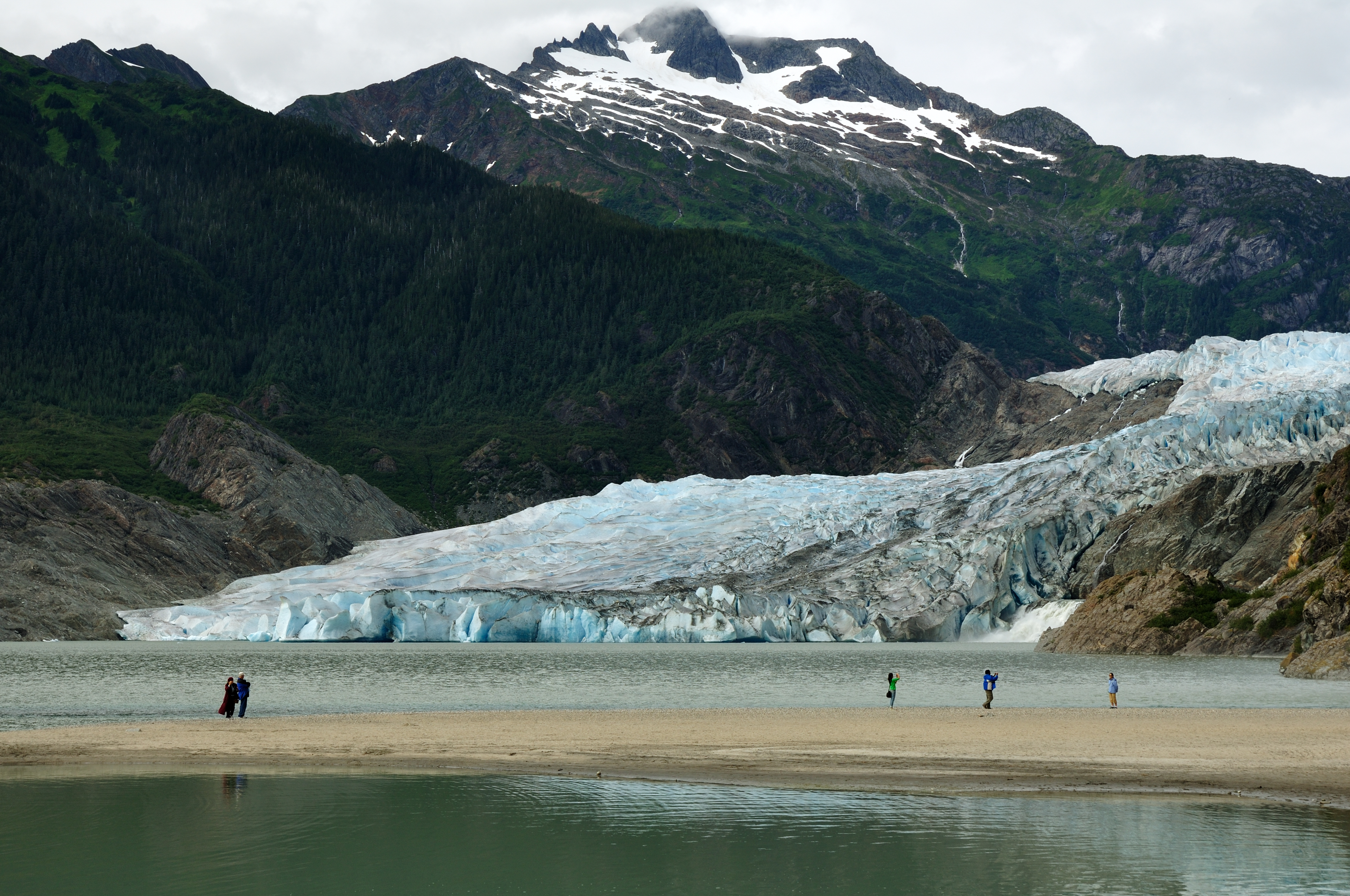 Turister udforsker Mendenhall Gletsjer strand i Juneau Alaska med sne-dækkede bjerge